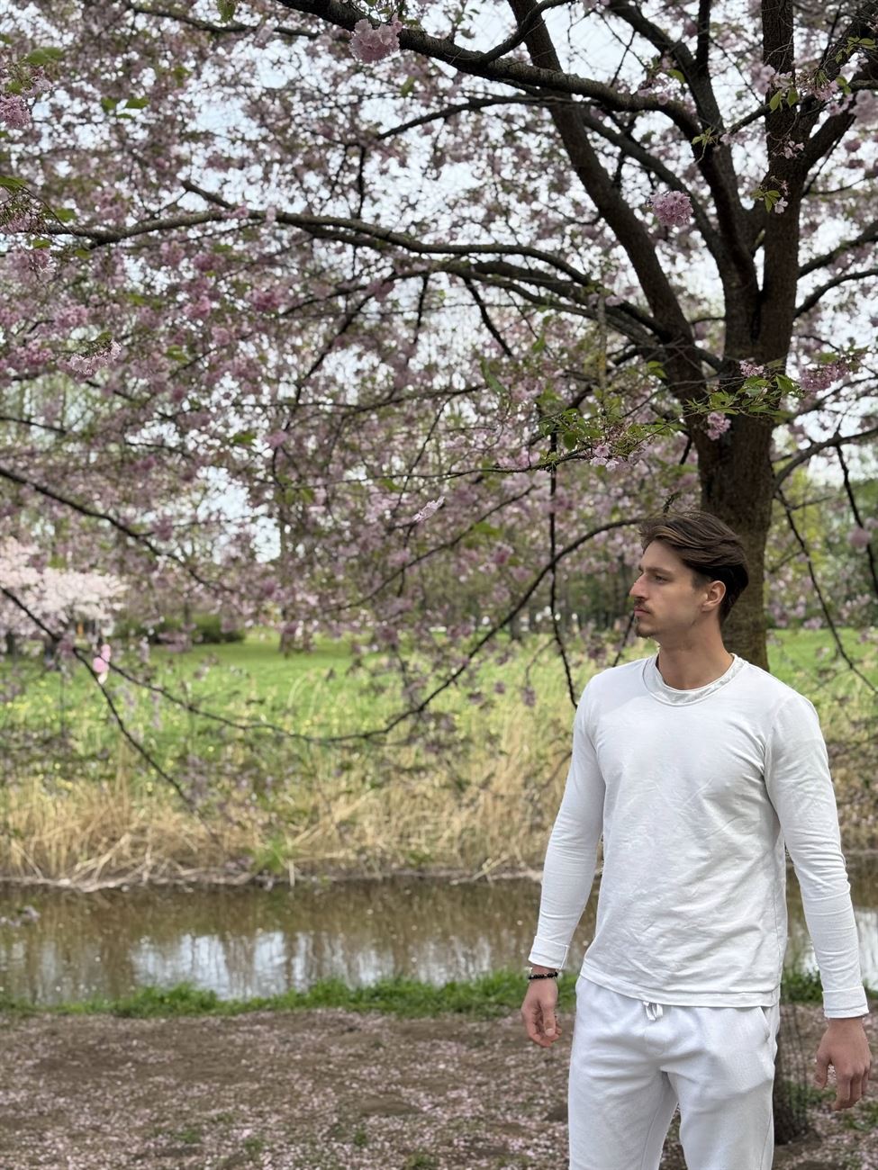Rinalds Dērics, portrait in a white outfit at a cherry-blossom park